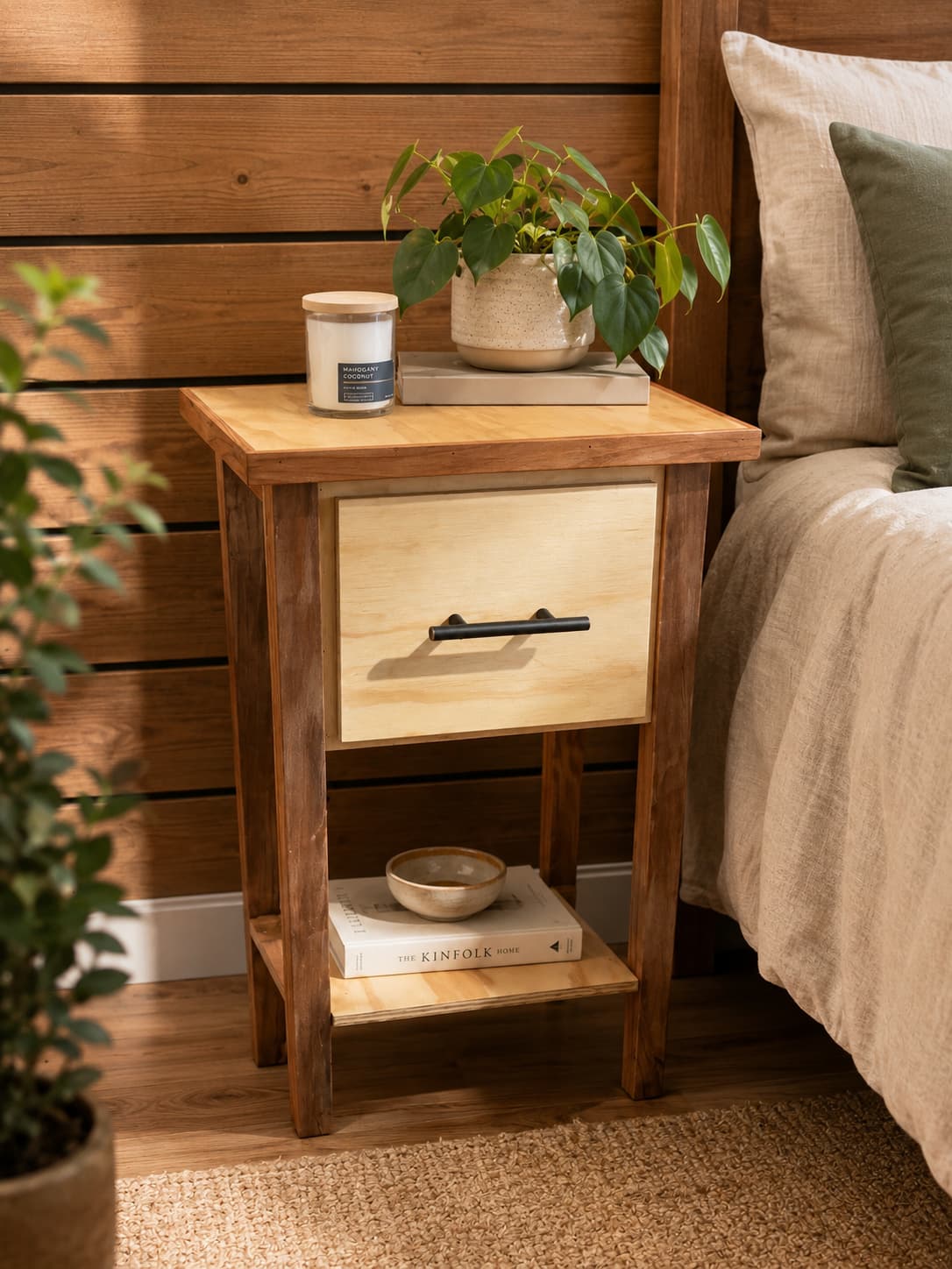 A wooden bedside table styled next to a bed with a plant and books